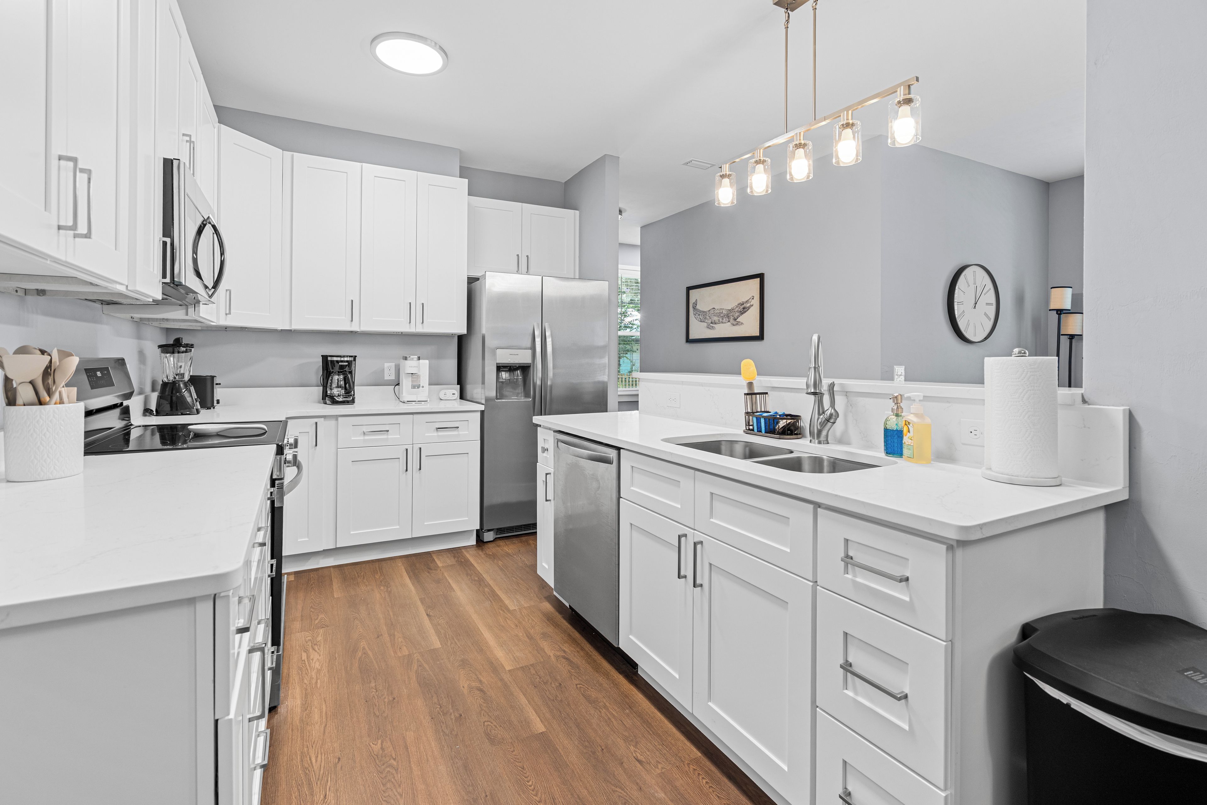 A modern kitchen with white cabinetry, a stainless steel refrigerator, a built-in oven, a coffee maker, and a sink.