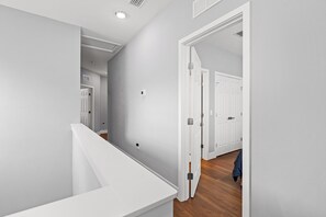 A hallway with white walls, a wooden floor, and a white door leading to another room. - 7 MINUTES TO CAMPUS! (Gainesville)