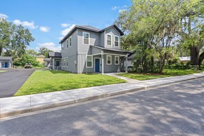 A two-story residential house with a front porch, a garage, and a well-maintained lawn. - 7 MINUTES TO CAMPUS! (Gainesville)