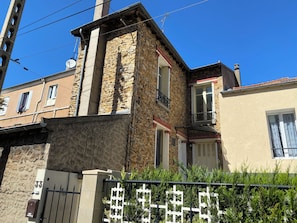 Un immeuble d’angle avec une façade en pierre, un portail en métal et un petit balcon.