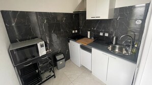 A compact kitchen with a black marble backsplash, white cabinets, a stainless steel sink, and a small trash bin. - Cozy, near Paris (Villeneuve-Saint-Georges)