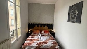 A narrow hotel room with a bed, a headboard, a wall-mounted artwork, and a window. - Cozy, near Paris (Villeneuve-Saint-Georges)