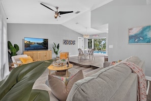 A modern living room with a flat-screen TV, a ceiling fan, and a view of a pool. - VILLA CORAL CABANA – HEATED POOL | WATER VIEW | PUTTING GREEN | BOAT RENTAL + TOURS VOUCHER INCL. (Cape Coral)