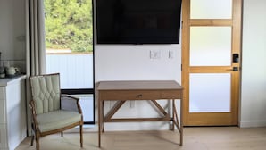 A room with a wooden table, a wicker chair, a television mounted on the wall, and a door with a frosted glass panel. - Charming studio in quiet neighborhood with great views. 10 minutes from beaches (Encinitas)