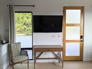A room with a wooden table, a wicker chair, a television mounted on the wall, and a door with a frosted glass panel.