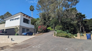 A two-story house with a garage, parked cars, and a driveway leading to a street. - Charming studio in quiet neighborhood with great views. 10 minutes from beaches (Encinitas)