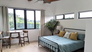 A bedroom with a bed, a table with chairs, a ceiling fan, and a window with curtains. - Charming studio in quiet neighborhood with great views. 10 minutes from beaches (Encinitas)