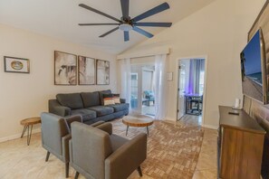 Ein Wohnzimmer mit einer Couch, Sesseln, einem Couchtisch, einem Deckenventilator und einem Fernseher.