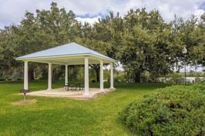 Ein Pavillon mit blauem Dach und weißen Säulen, umgeben von Gras und Bäumen.