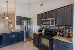 A modern kitchen with dark cabinetry, stainless steel appliances, a granite countertop, and a backsplash with a mosaic tile pattern. - Peaceful 3BR 2BTH Villa | Private Pool | Game Room | Champions Gate Area (Davenport)