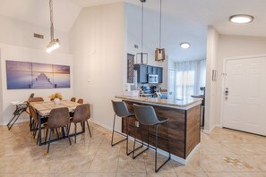 Une cuisine moderne avec des meubles de couleur sombre, un îlot central et des luminaires suspendus.