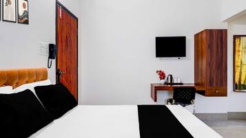 A hotel room with a bed, a desk with a chair, a television, and a wooden wardrobe.