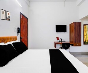 A hotel room with a bed, a desk with a chair, a television, and a wooden wardrobe. - Deluxe Brahmaputra View (Chandanpur)