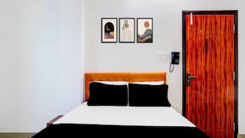 A hotel room with a bed, a wooden door, and three framed pictures on the wall.