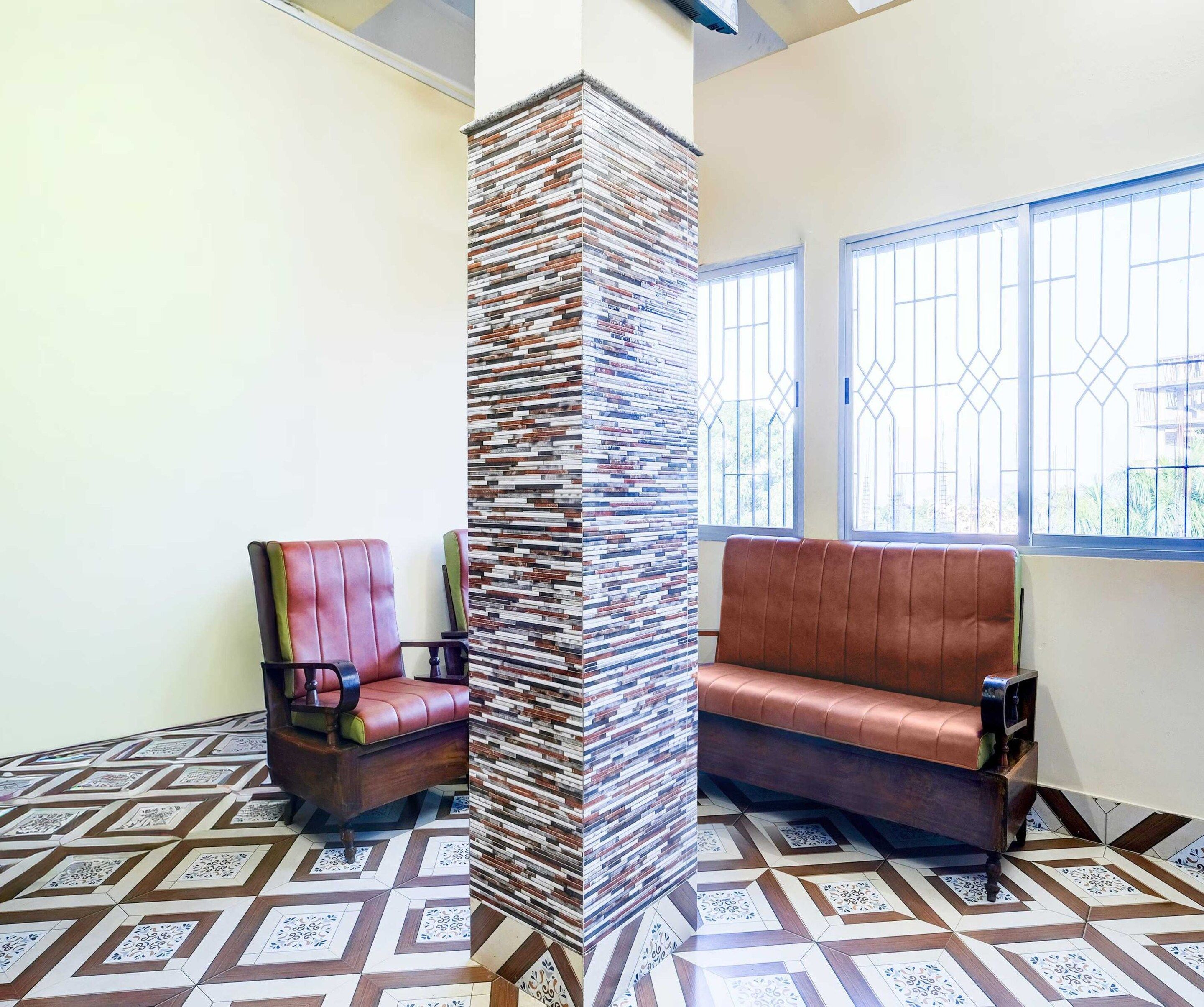 A room with a patterned floor, a tall pillar, a cushioned bench, and a chair.