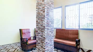 A room with a patterned floor, a tall pillar, a cushioned bench, and a chair.