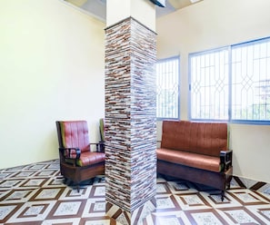 A room with a patterned floor, a tall pillar, a cushioned bench, and a chair. - Deluxe Brahmaputra View (Chandanpur)