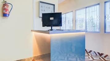 A reception desk with a flat-screen TV, a fire extinguisher, and patterned floor tiles.