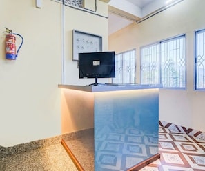 Un mostrador de recepción con un televisor de pantalla plana, un extintor y baldosas de suelo con diseño.