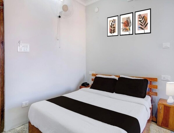 Ein Schlafzimmer mit einem Bett, einem Nachttisch, einer Lampe und drei gerahmten Kunstwerken an der Wand.