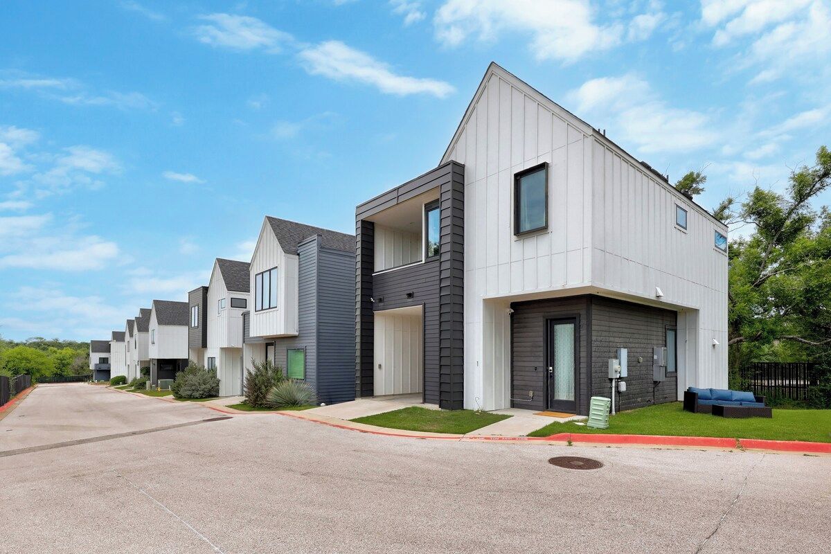 A row of modern townhouses with a flat roof, large windows, and a well-maintained lawn.