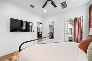 Ein Schlafzimmer mit einem Bett, einem an der Wand montierten Fernseher, einem Deckenventilator und einer Tür zu einem Außenbereich.