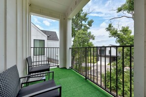 Ein Balkon mit einem grünen Kunstrasenteppich, einem schwarzen Metallgeländer und einem weißen Gebäude im Hintergrund.