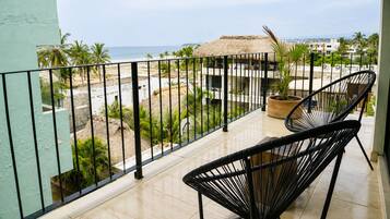 A balcony with two black wicker chairs, a potted plant, and a view of the beach and ocean.