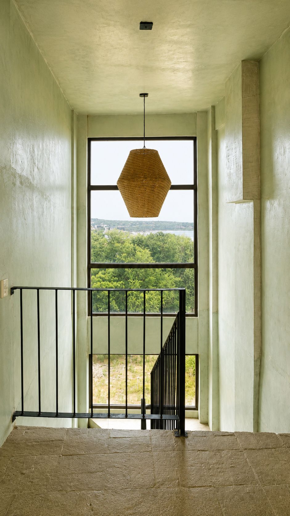 Una escalera con vistas a la vegetación exterior, una lámpara colgante y una barandilla de metal.