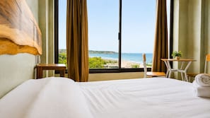A hotel room with a large bed, a view of the beach, a small table, and a chair. - CASA AMOR ZIKATELA (Santa Maria Colotepec)