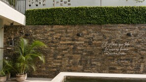 A stone wall with a quote in Spanish, a potted palm plant, and a pool. - CASA AMOR ZIKATELA (Santa Maria Colotepec)