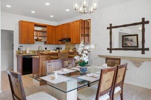 A modern kitchen with wooden cabinets, a glass dining table, and a chandelier. - Kapalua 14T3 | Spacious 3BR Maui Vacation Home (Lahaina)
