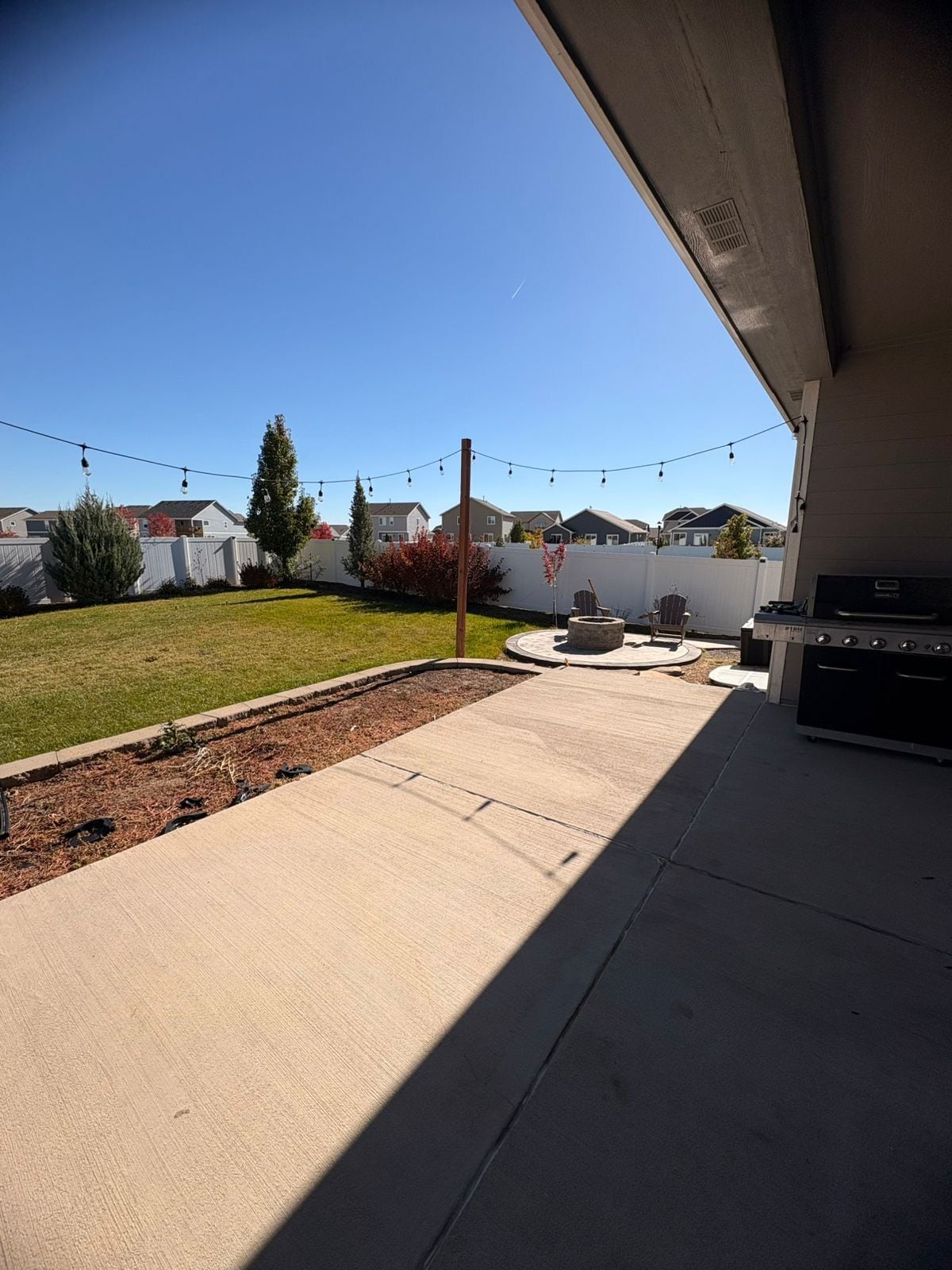 Un patio trasero con una parrilla, mobiliario exterior e iluminación colgante.