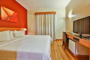Una habitación de hotel con cama, escritorio con televisor y ventana con cortinas.