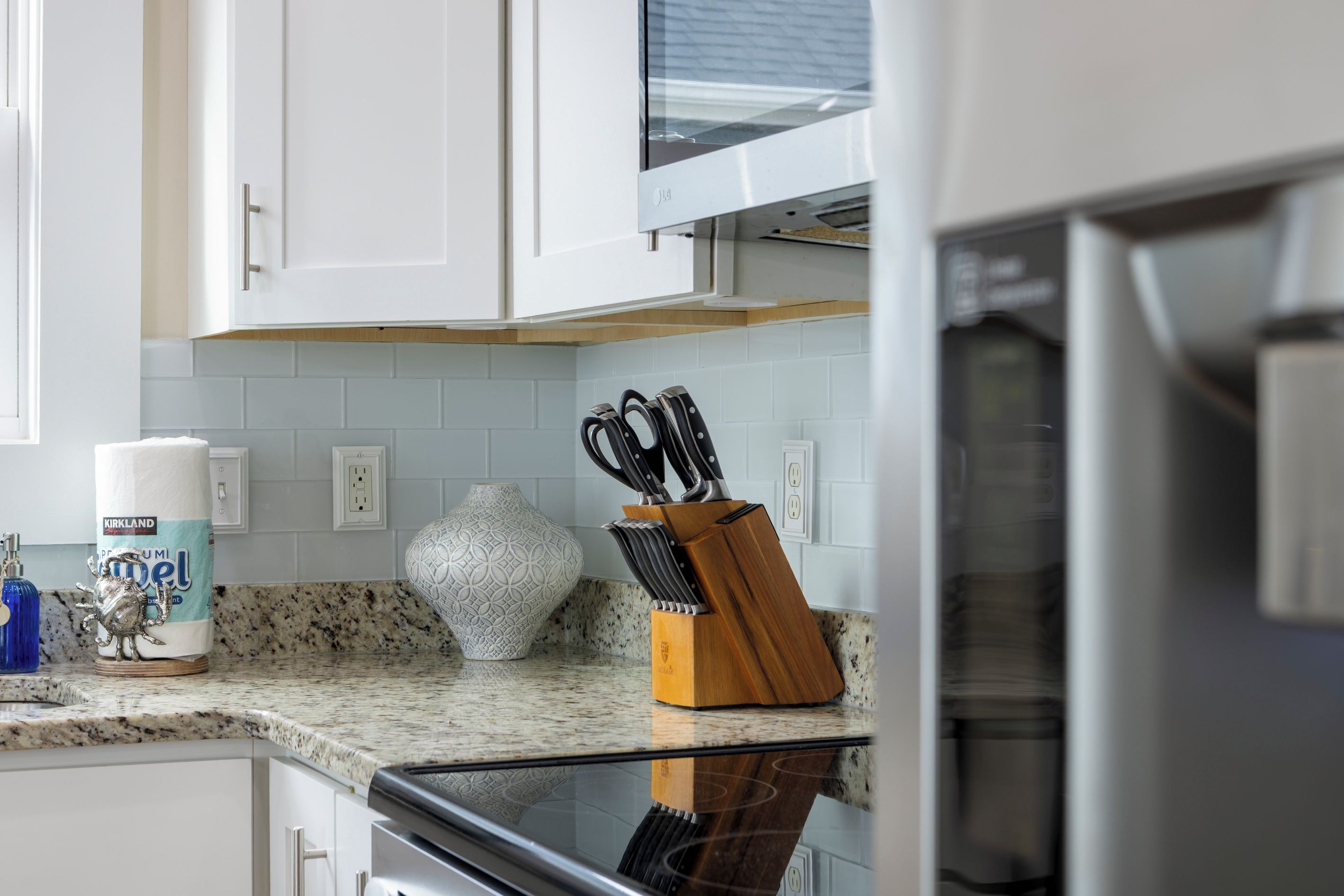 A kitchen with white cabinets, a granite countertop, a decorative vase, and a knife block.