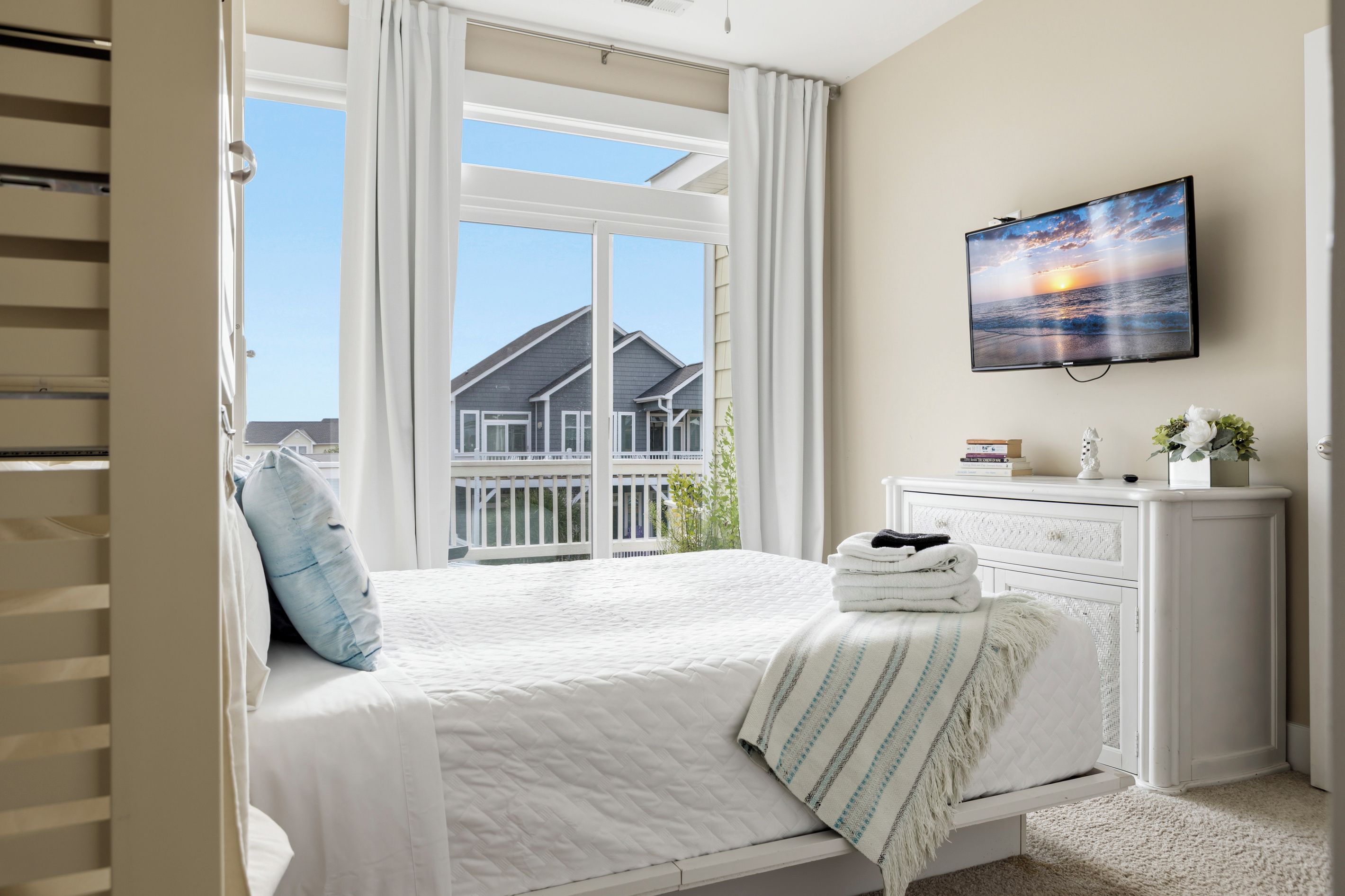 Une chambre à coucher avec un lit, une table de chevet, un téléviseur et une vue sur une maison par la fenêtre.