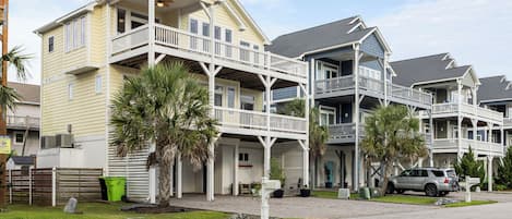 A beachfront hotel with multiple balconies, a covered outdoor seating area, and a parking lot.