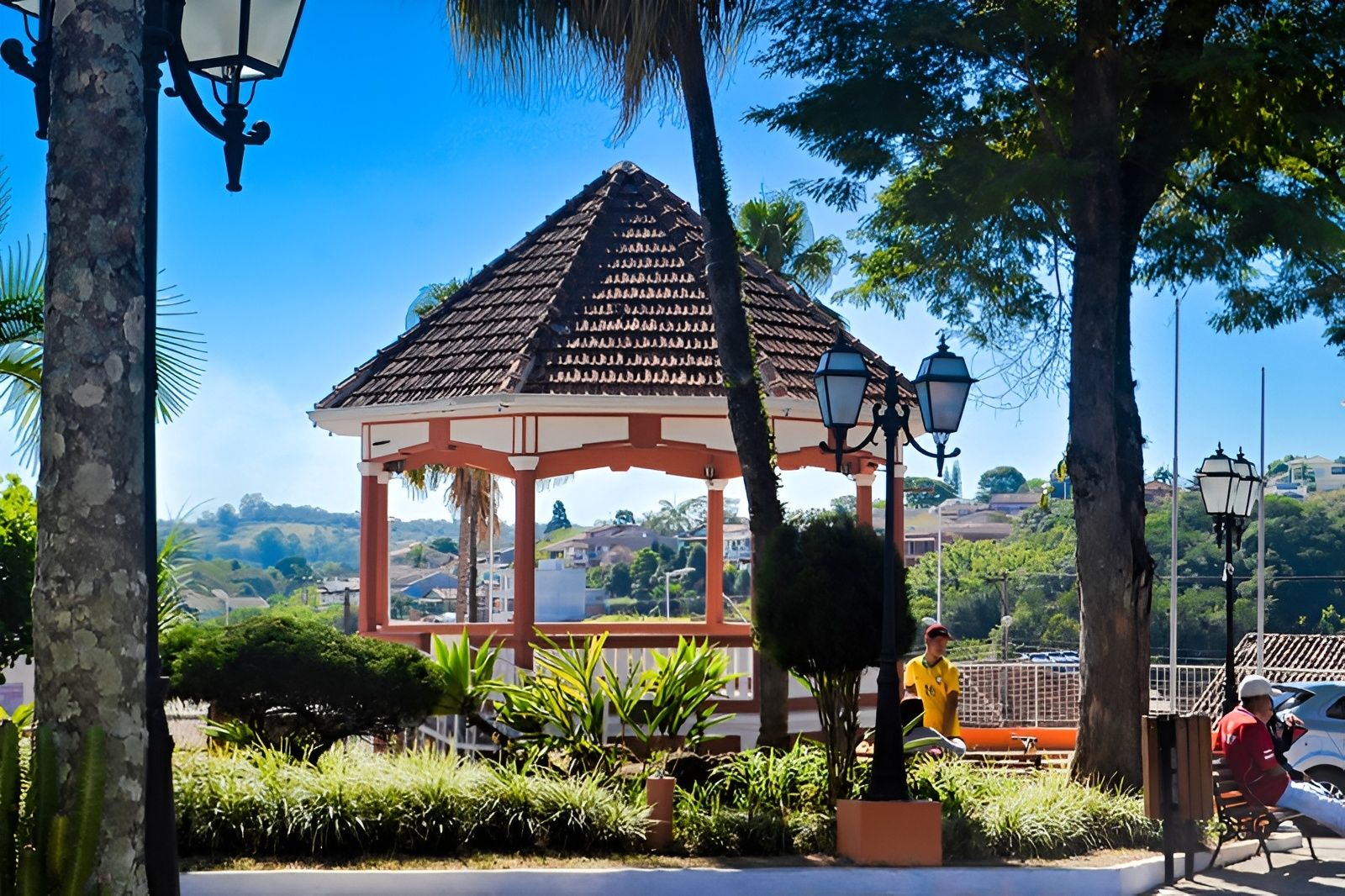 Um gazebo com telhado ladrilhado, rodeado por vegetação e postes de iluminação.
