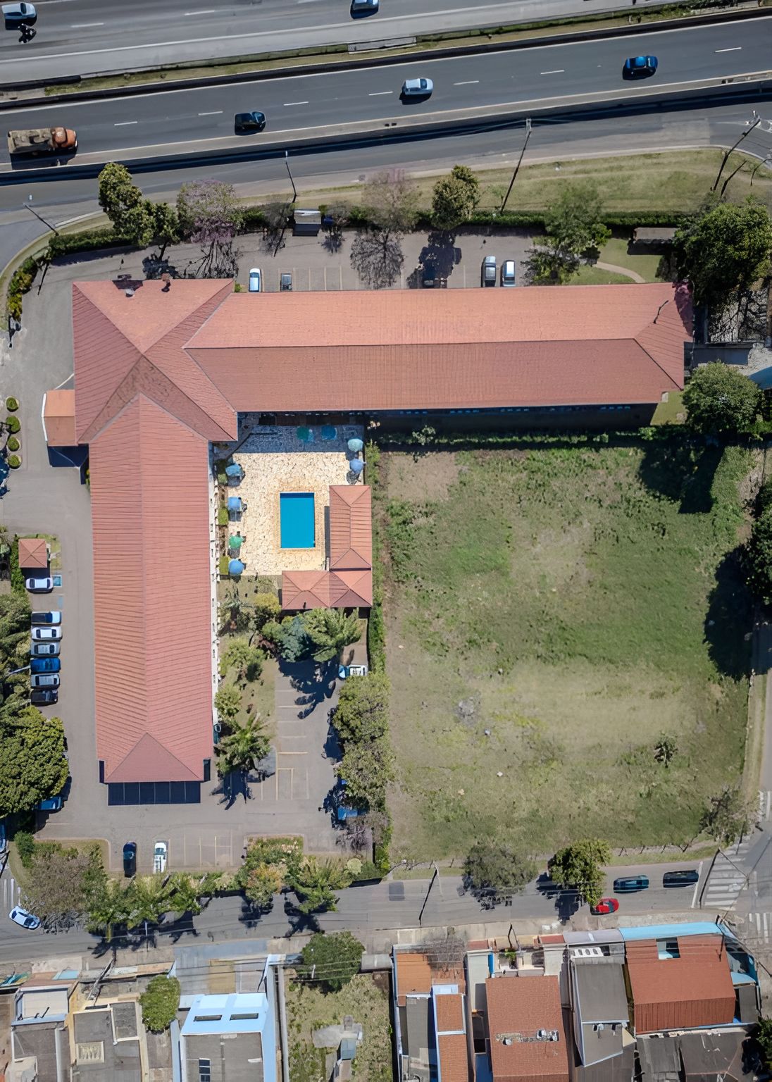 Vista aérea de um edifício com um amplo estacionamento, piscina e área gramada.
