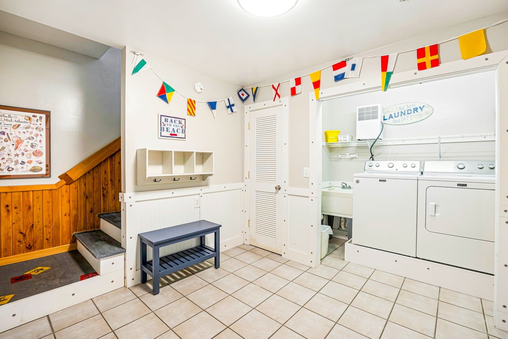 Una sala de lavandería con una lavadora, una secadora y una pequeña mesa. Hay un letrero en la pared que dice 'BACK TO THE BEACH'.