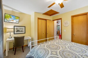 Un dormitorio con cama, escritorio, silla, ventilador de techo y dos puertas.