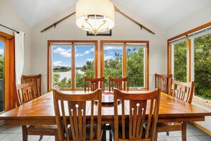 A dining area with a large table and chairs, large windows with a view of a lake, and a modern chandelier. - Turtle's Cove Corolla retreat with beach access, hot tub, and views. (Corolla)