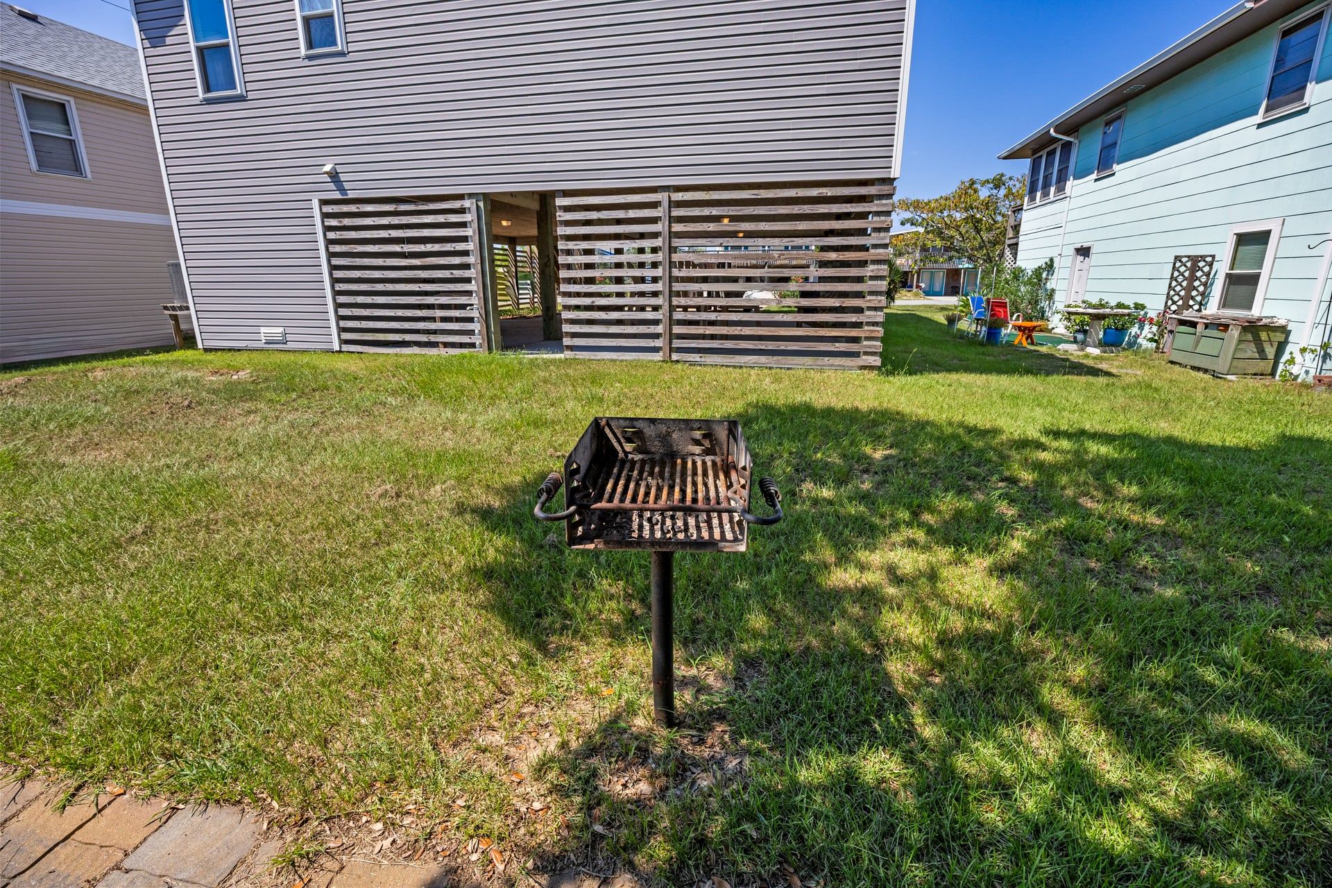 A backyard with a grill, a wooden fence, and a house with a window.