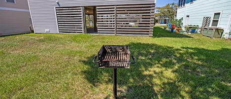 A backyard with a grill, a wooden fence, and a house with a window.