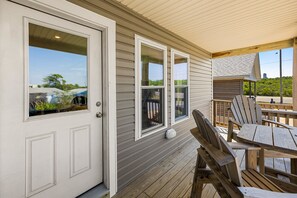 A covered porch with wooden furniture and a door with glass panels. - Sandy Paws hot tub, fenced yard, and beach access. (Kill Devil Hills)
