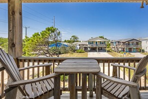 A wooden deck with a table and chairs, overlooking a residential area with houses and a clear sky. - Sandy Paws hot tub, fenced yard, and beach access. (Kill Devil Hills)