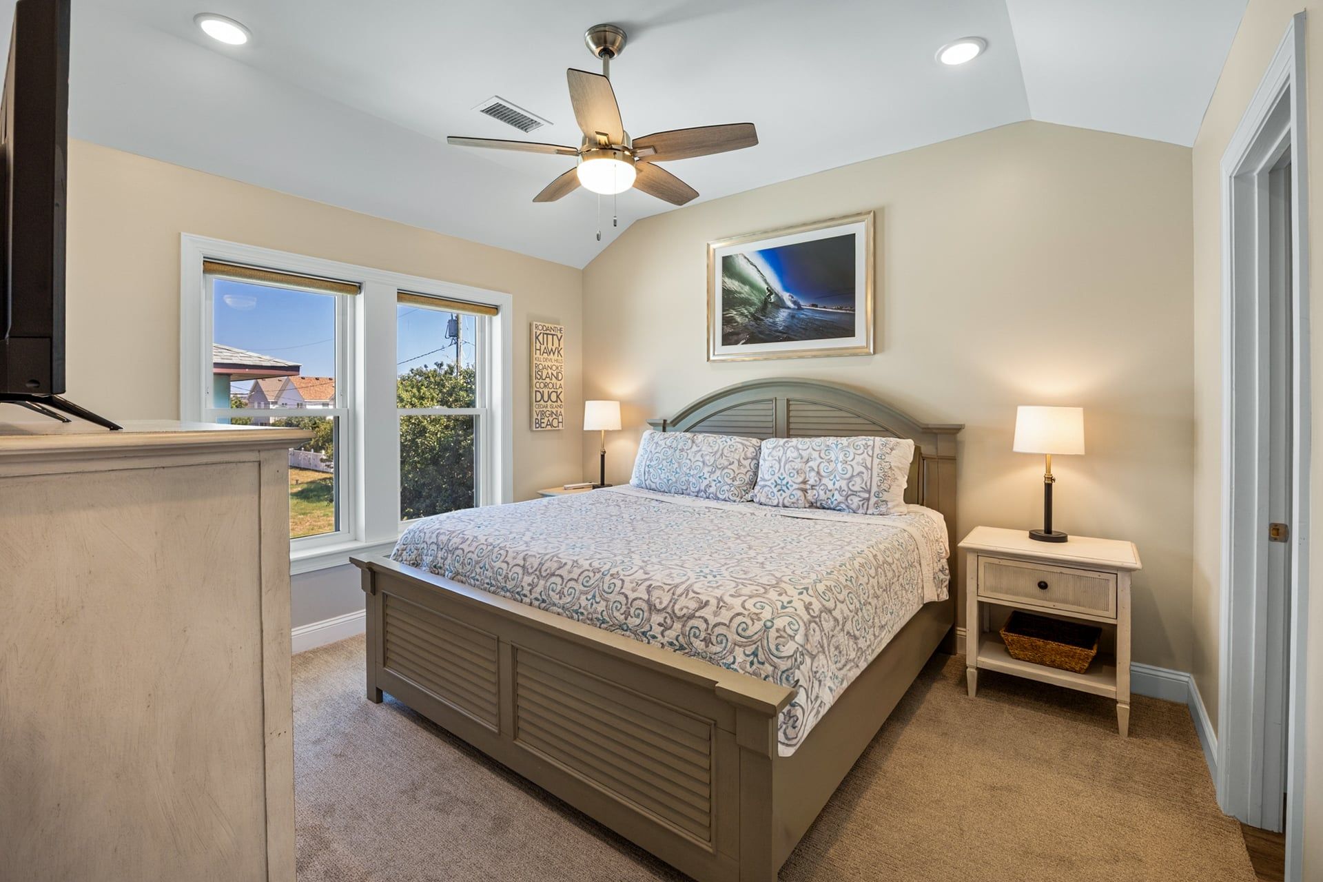 A bedroom with a bed, bedside lamps, a ceiling fan, a window, and a framed picture on the wall.