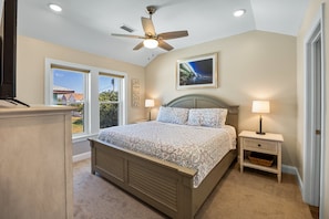 A bedroom with a bed, bedside lamps, a ceiling fan, a window, and a framed picture on the wall. - Sandy Paws hot tub, fenced yard, and beach access. (Kill Devil Hills)