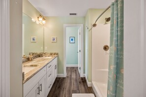 A bathroom with a vanity, a shower with a curtain, and a door leading to another room. - Sandy Paws hot tub, fenced yard, and beach access. (Kill Devil Hills)