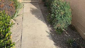 Une entrée fermée par un portail, avec un chemin en béton menant à un bâtiment aux murs recouverts d’enduit et doté d’un toit rouge.